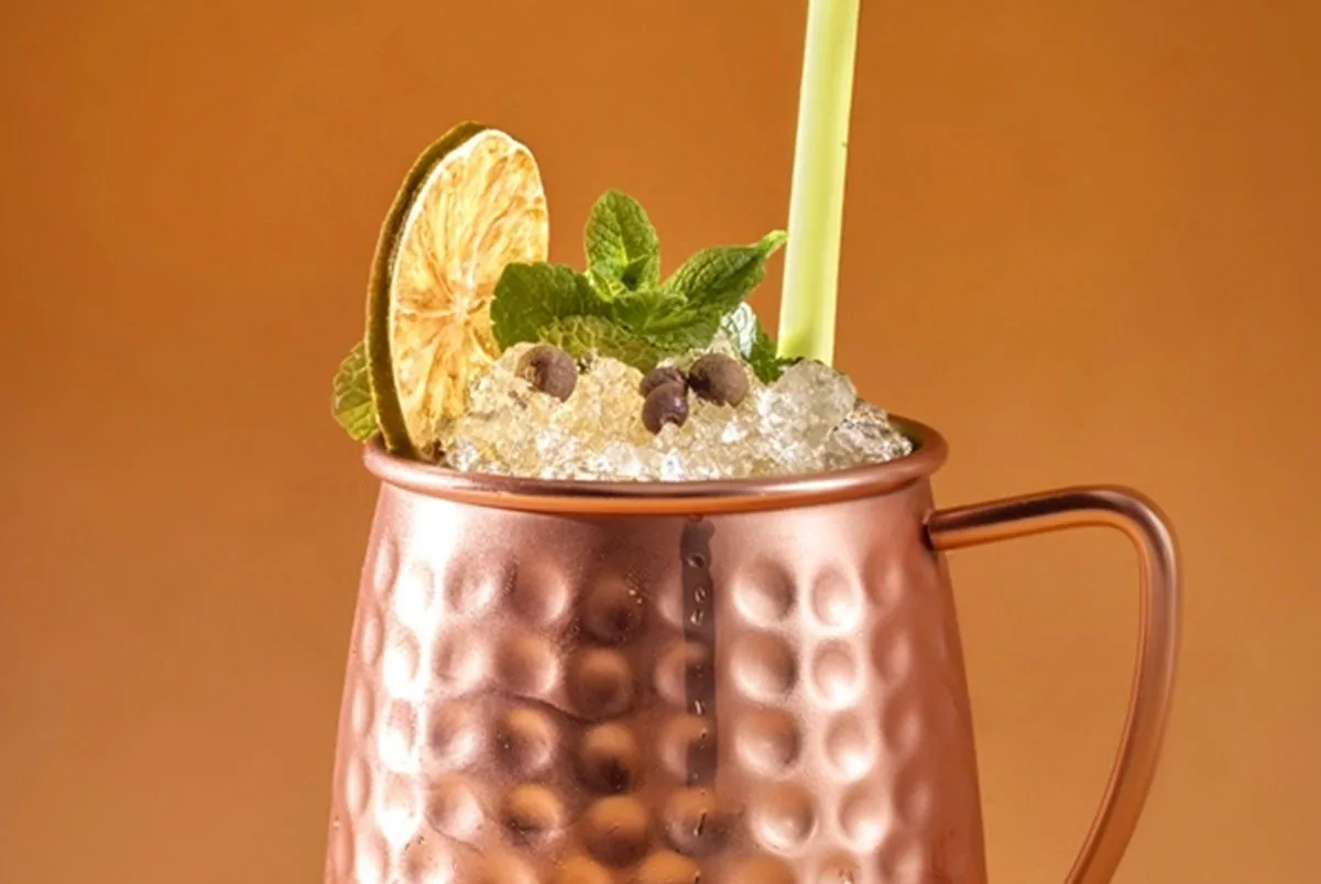 A copper mug cocktail garnished with mint and a lime wheel against an orange background