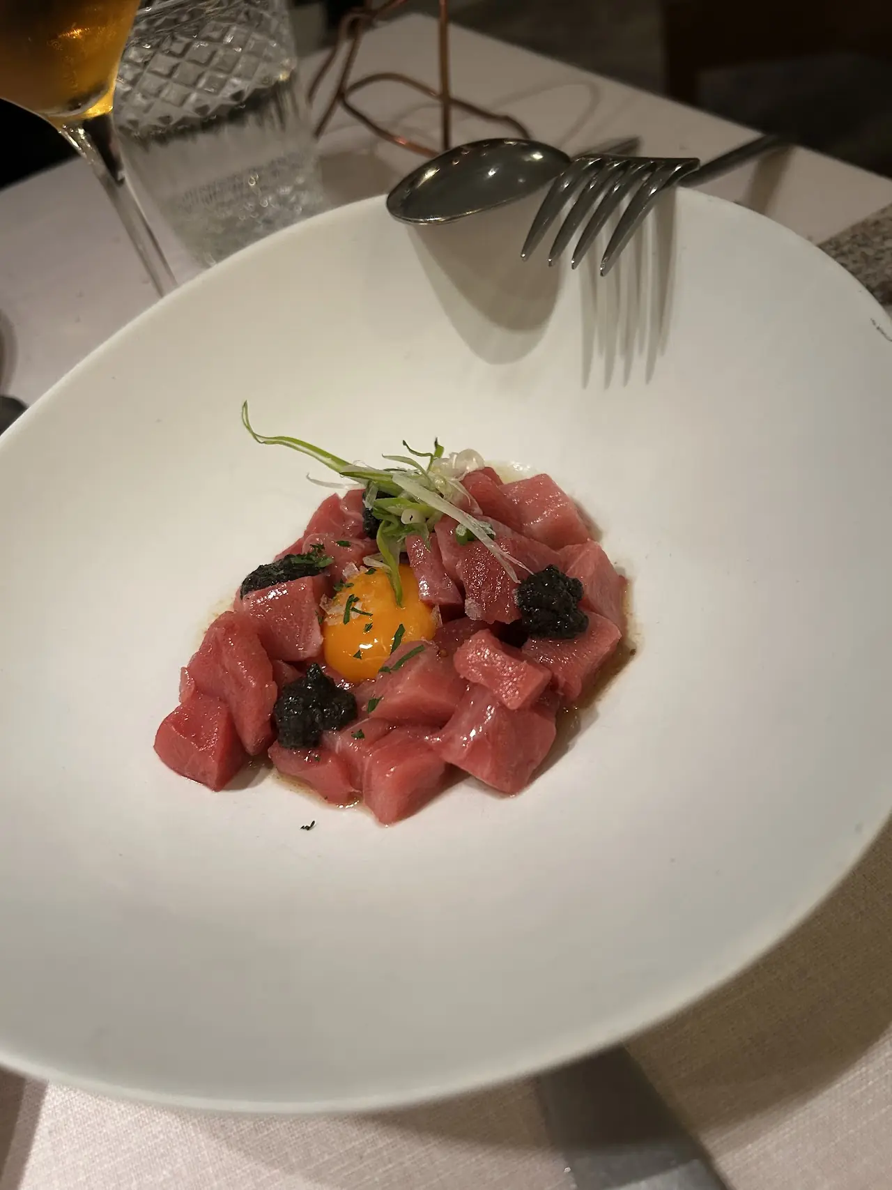 Thinly sliced raw beef tartare arranged on a white plate with herb garnish.