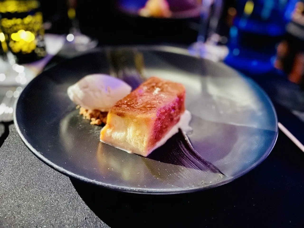 A dark plate with a pink and white dessert next to a scoop of ice cream