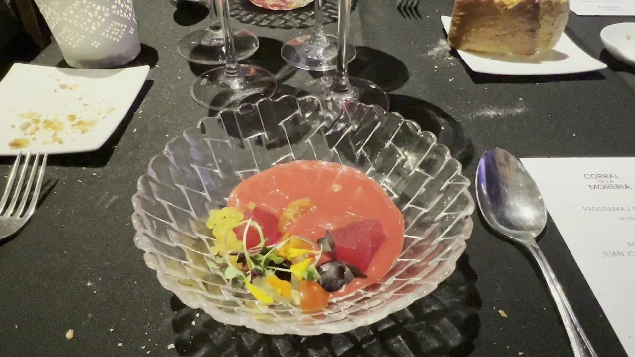 A clear glass bowl with a pink chilled soup and small yellow flowers