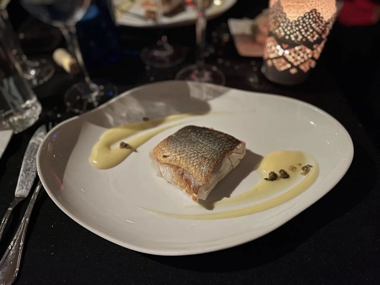 A fish fillet on a white plate with a swirl of cream sauce