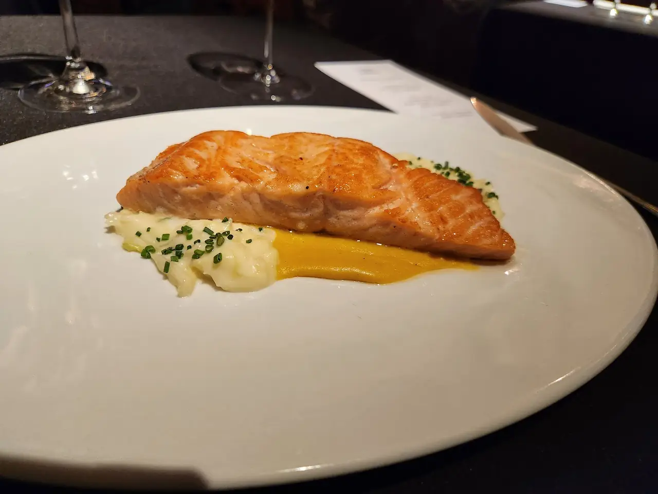 Seared salmon fillet over mashed potato with chives and a swirl of orange sauce on a white plate