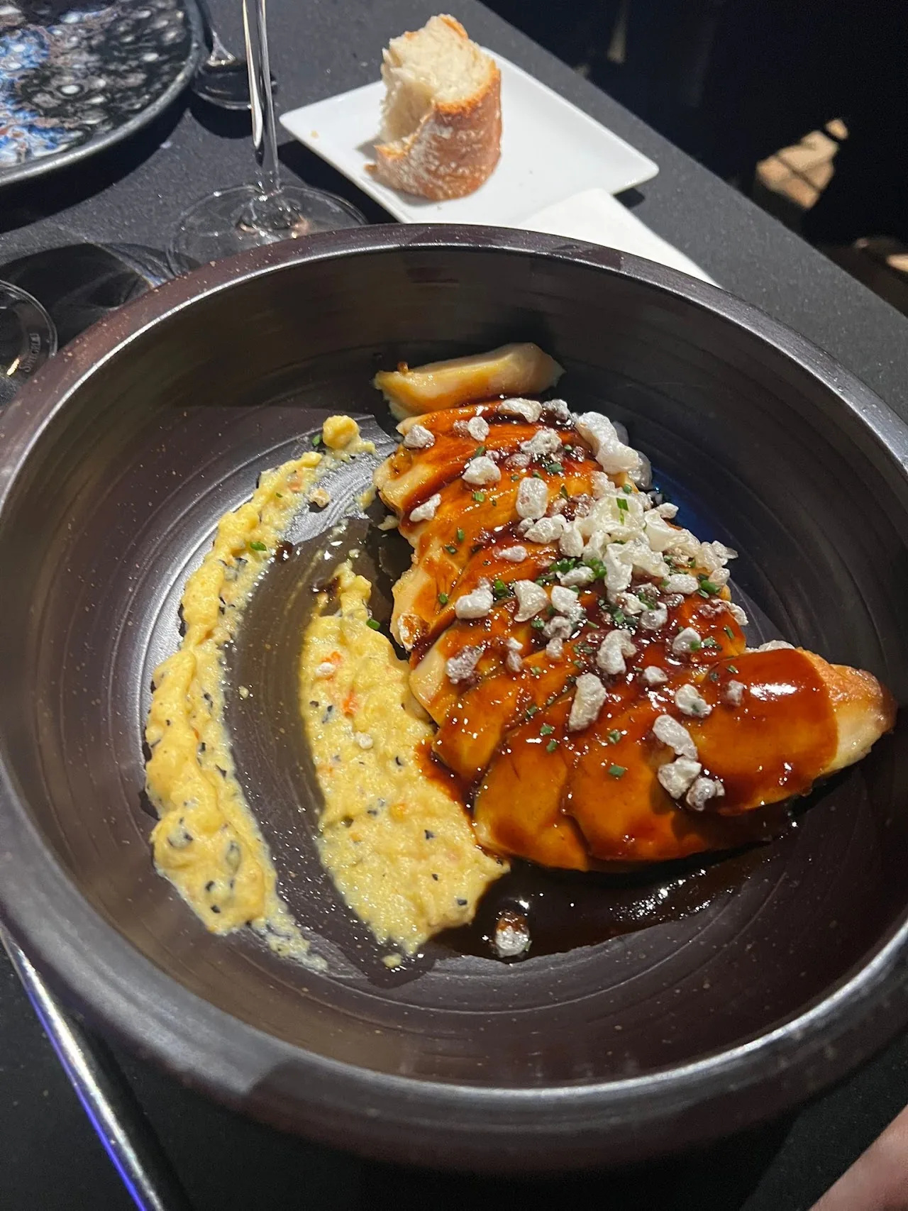 A dessert with caramel sauce, cream, and cheese crumble on a dark plate