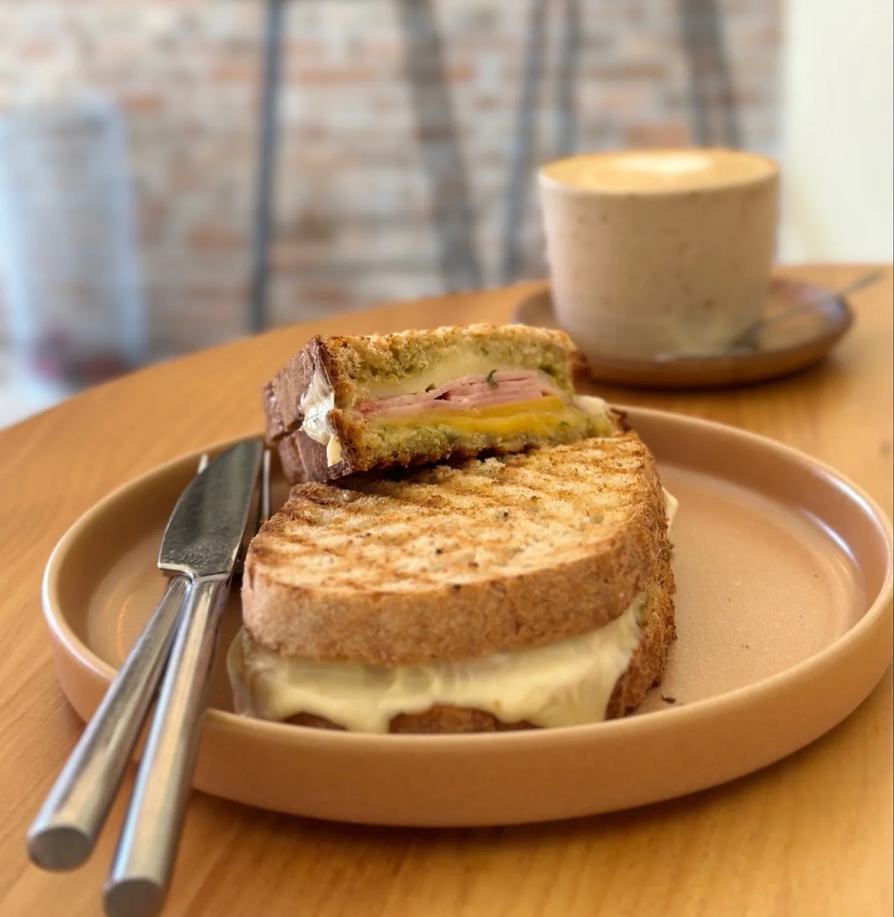 A toasted sandwich with melted cheese on a plate beside a coffee cup