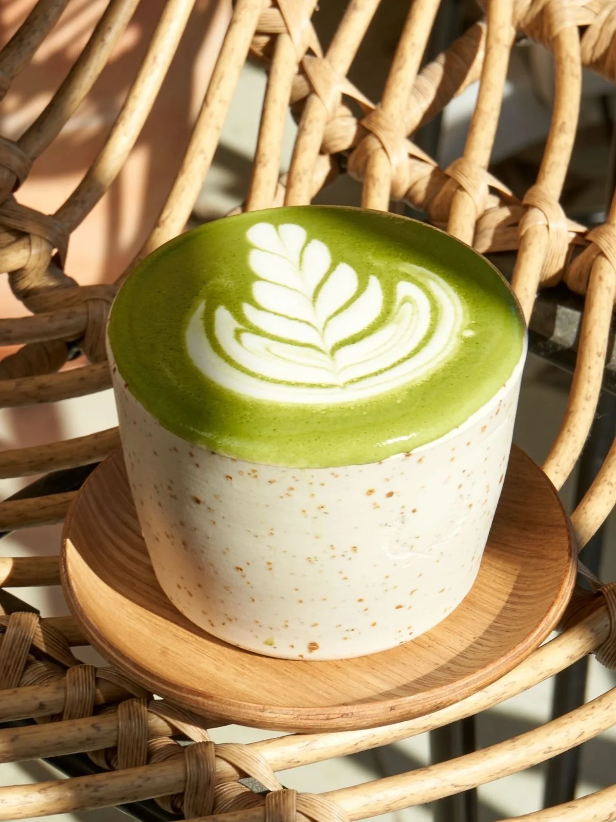 A matcha latte with leaf latte art in a speckled cup on a wooden saucer