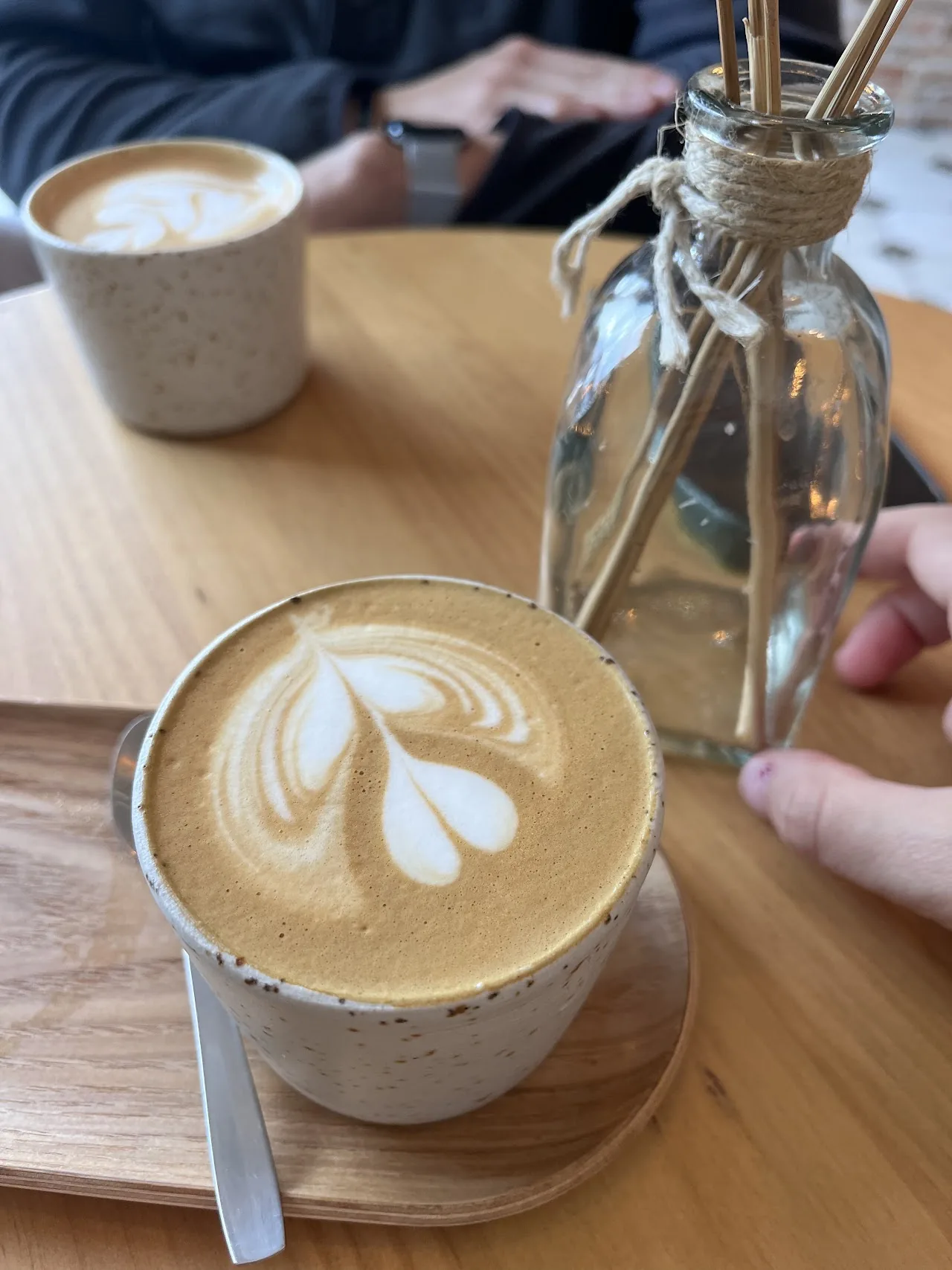 A latte with heart-shaped foam art next to a glass jar on a wooden table