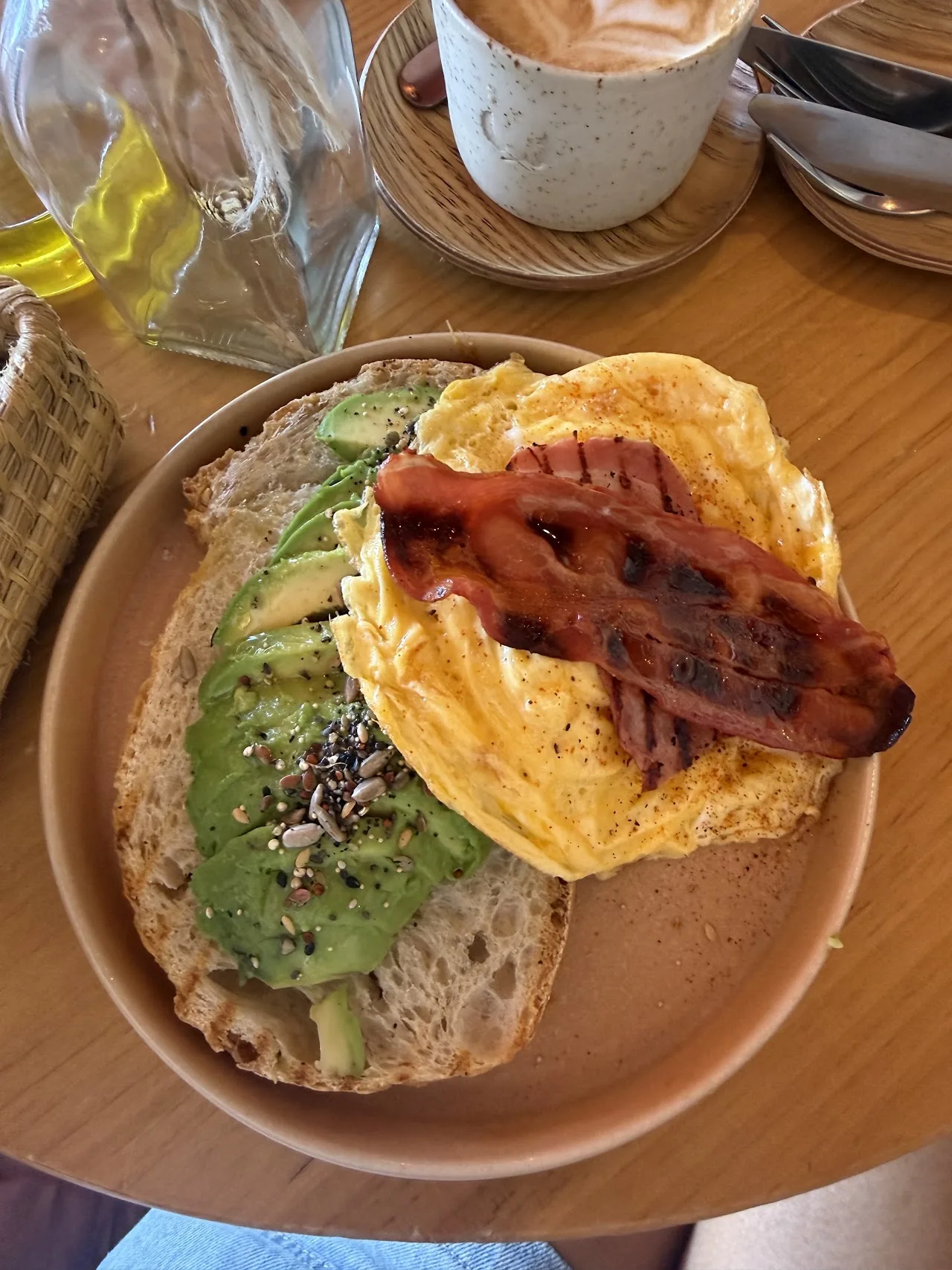An open-faced sandwich topped with avocado, crispy bacon, and seeds