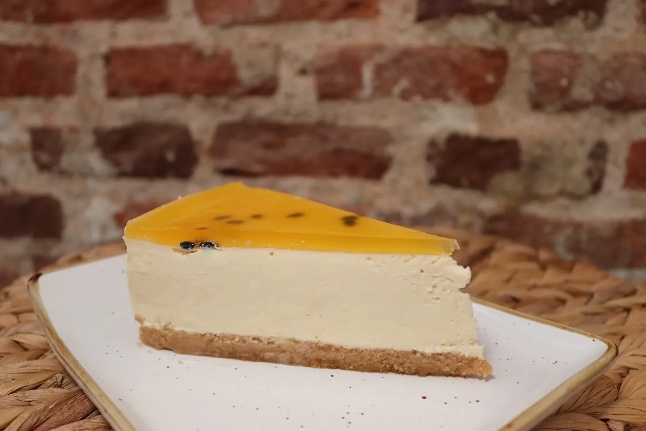 A slice of mango cheesecake on a plate against a brick wall