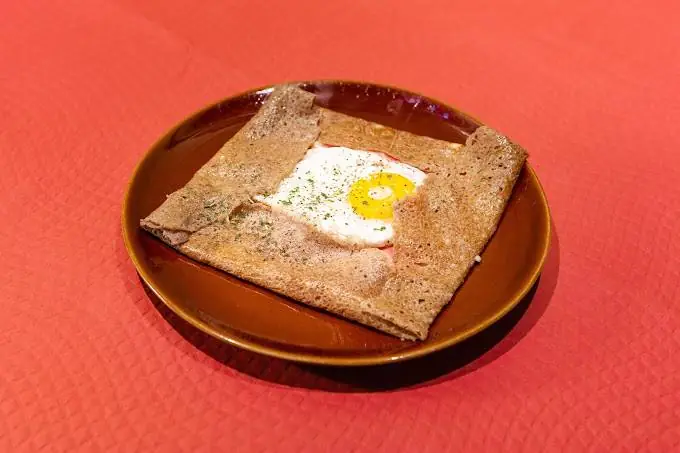 Square-folded buckwheat galette with a fried egg in the center on a brown plate, at Crêperie Les 3 Pommes