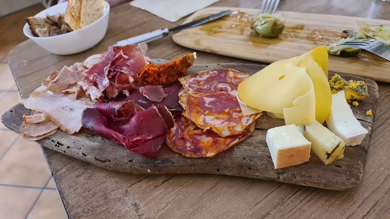 A wooden board of sliced cured meats, cheese and olives