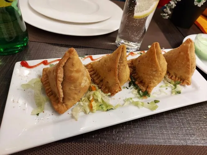 Four golden fried samosas arranged on a plate