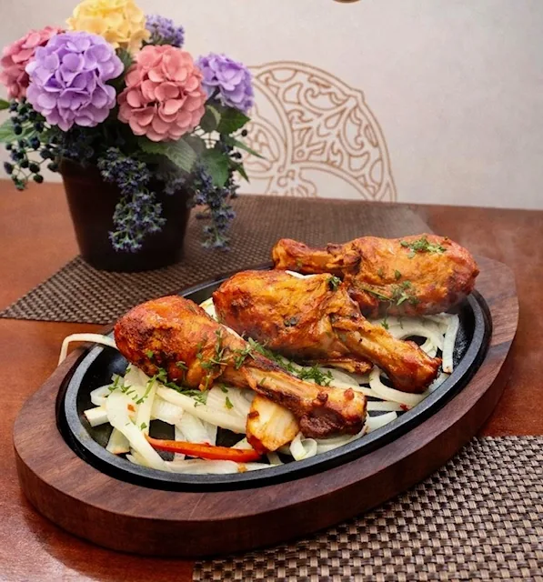 Tandoori chicken drumsticks served on a sizzling platter with onions