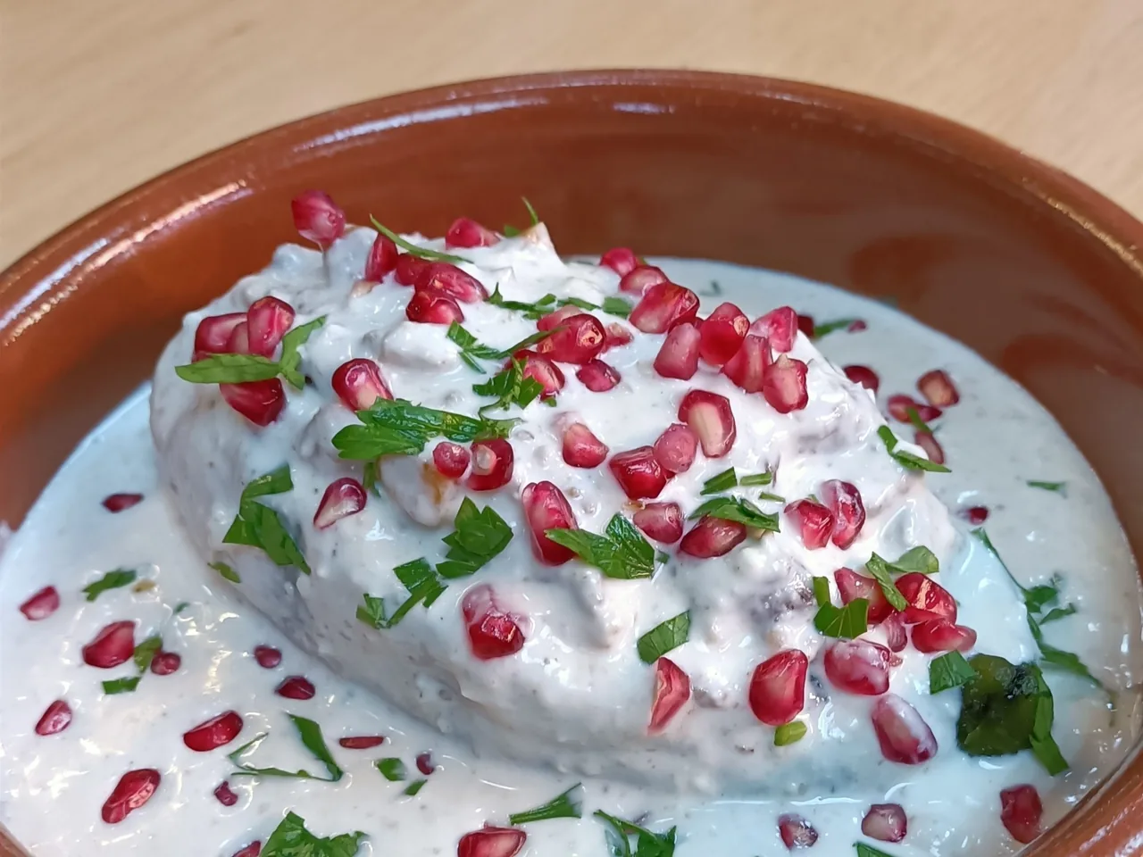 A terracotta dish with a stuffed pepper covered in white sauce and pomegranate seeds