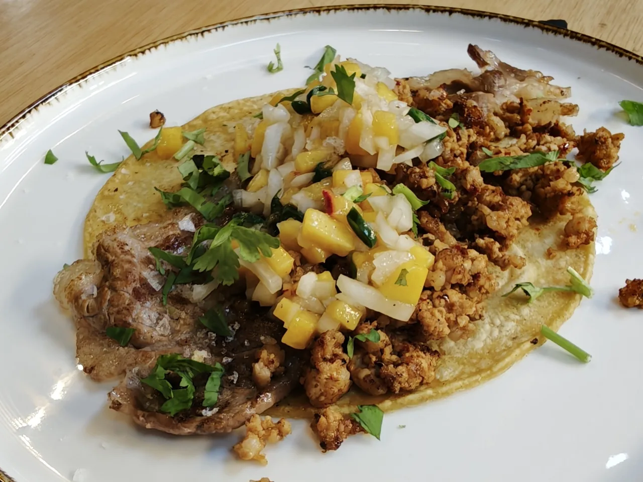 A taco topped with ground meat, diced vegetables and herbs on a white plate