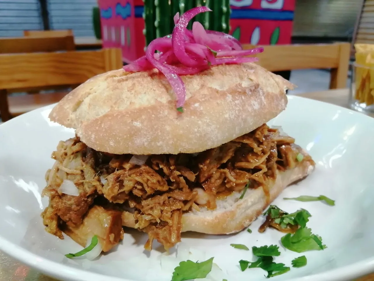 A pulled pork sandwich topped with pickled red onion on a soft roll