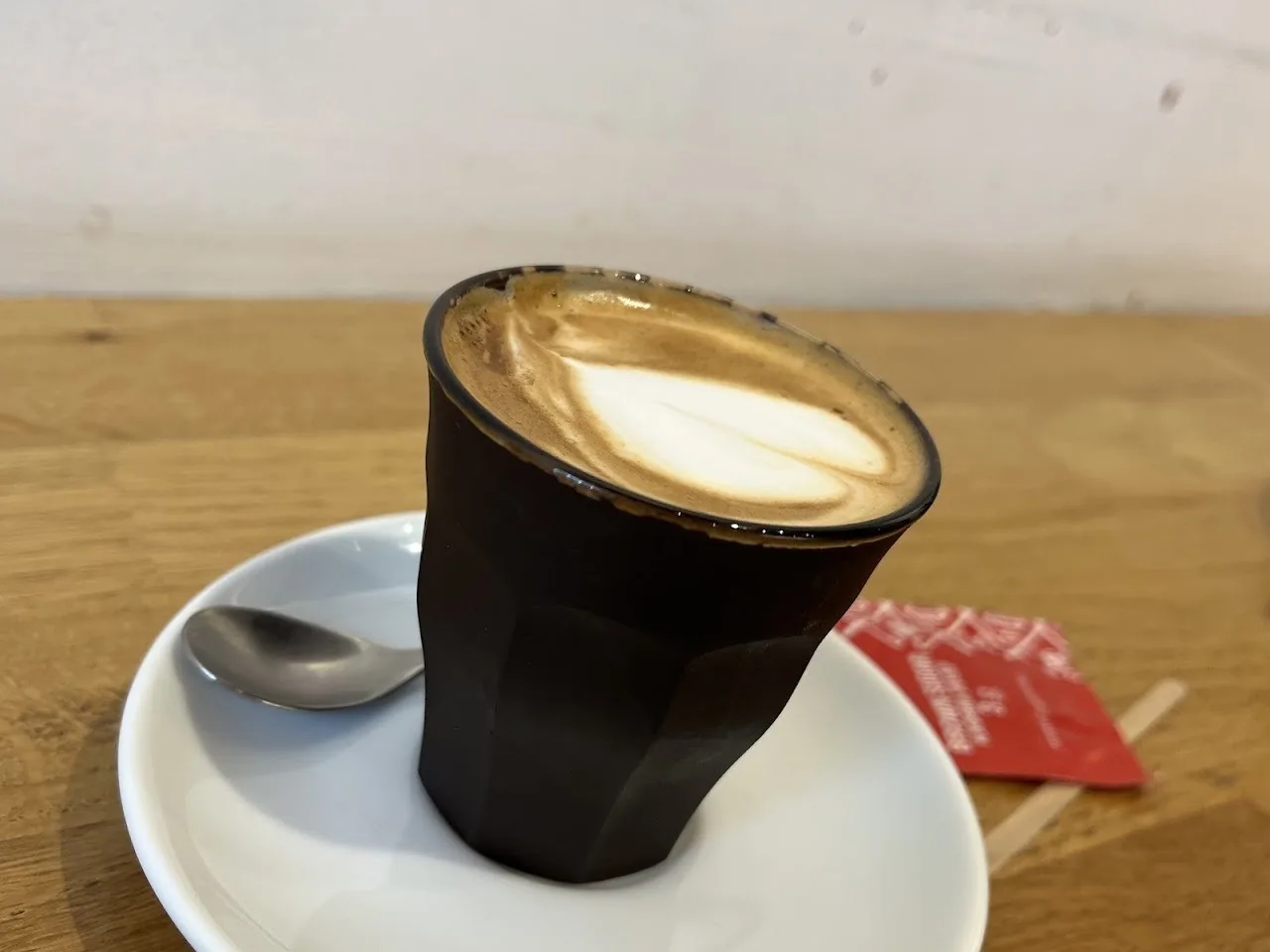 A coffee with milk in a small black glass on a white saucer