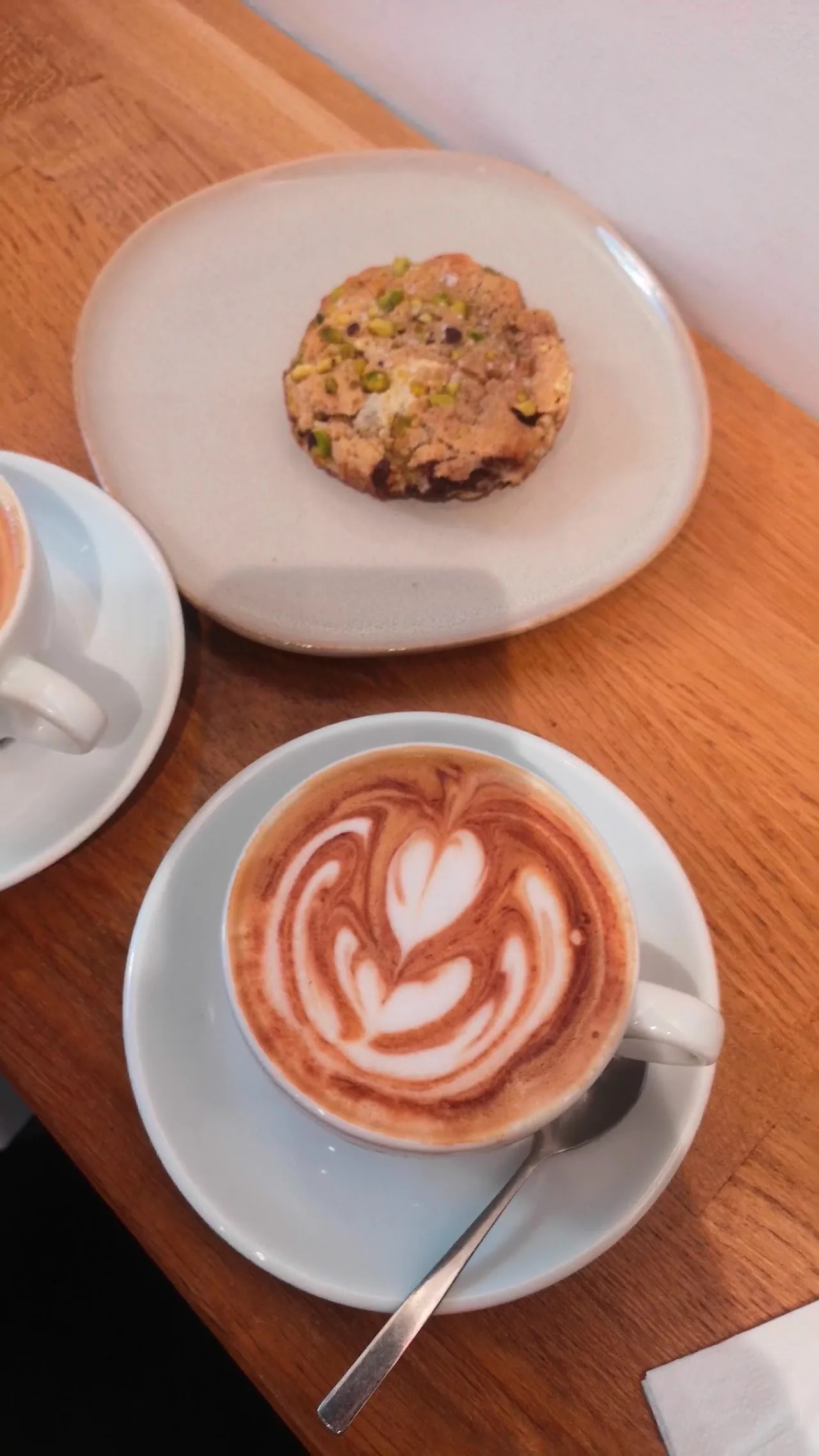 A latte with art in a cup beside a plate with a cookie on a wooden table