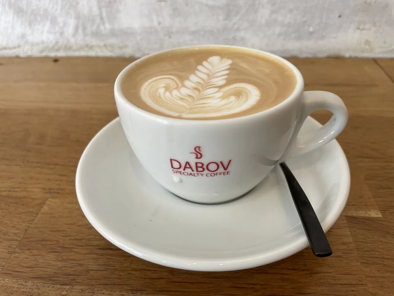 A latte with leaf-pattern foam art in a Dabov-branded cup