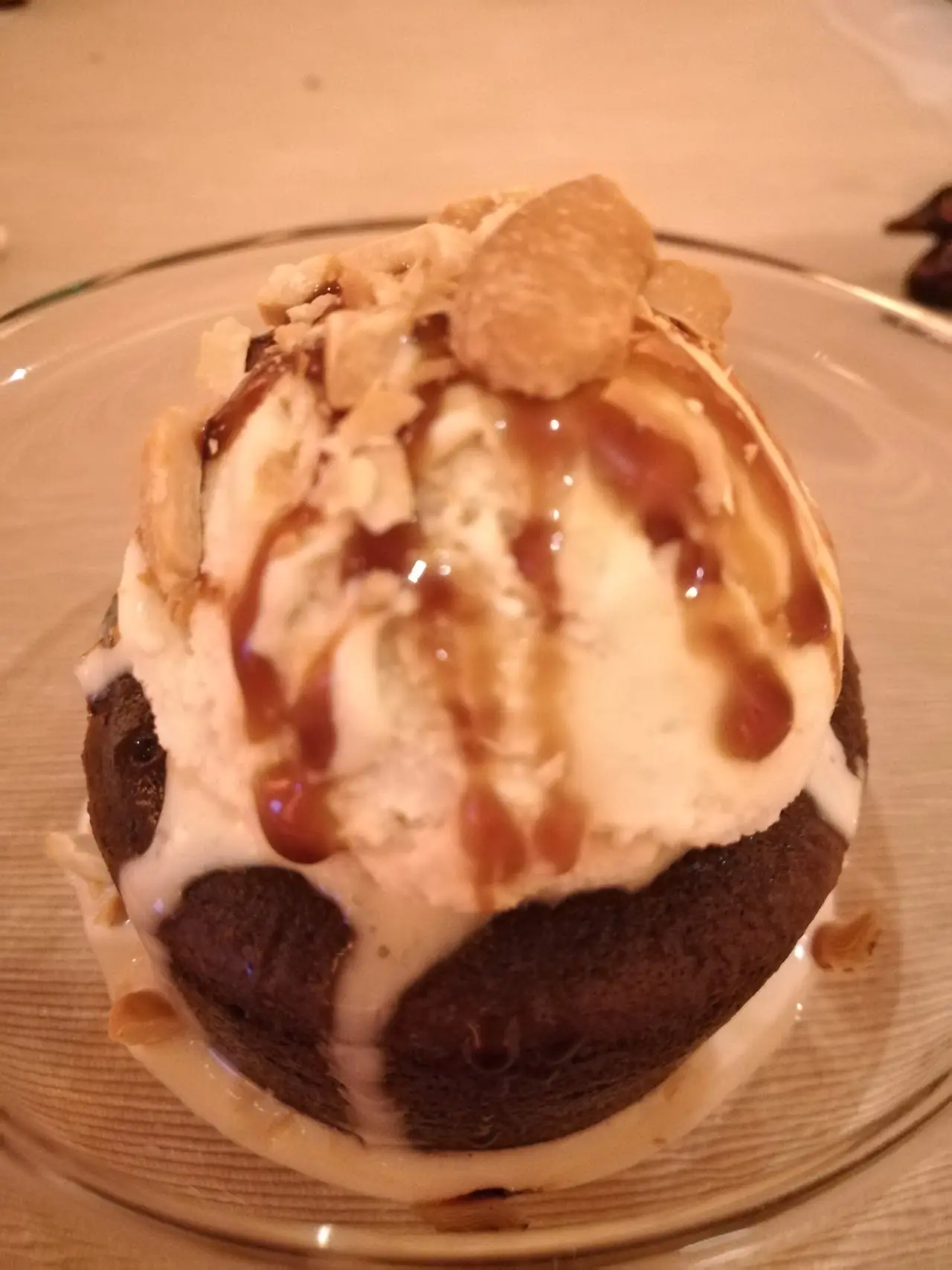 A round chocolate dessert with a scoop of ice cream, caramel drizzle, and a thin wafer garnish.