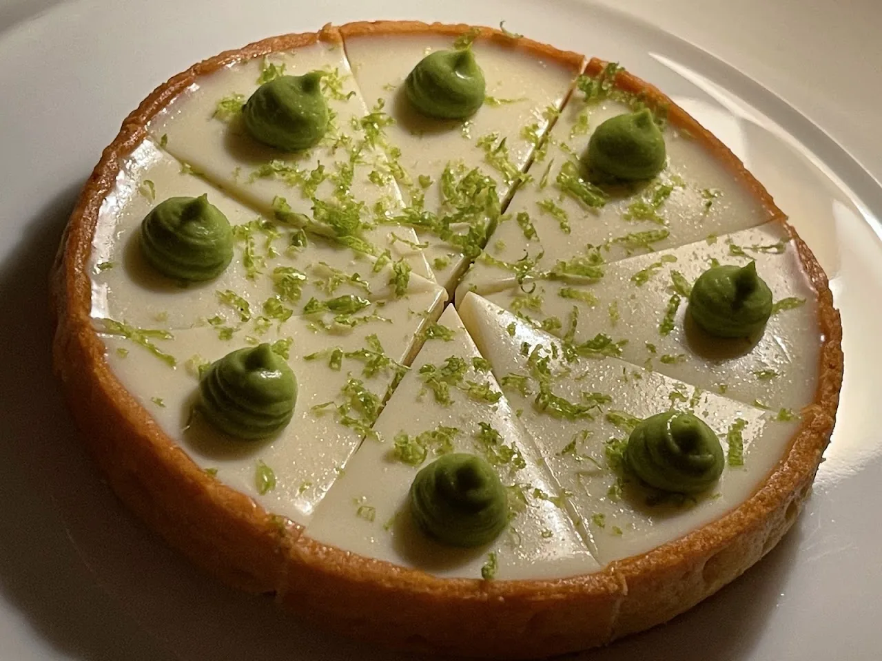 A lime tart with dollops of green cream on top, cut into wedges