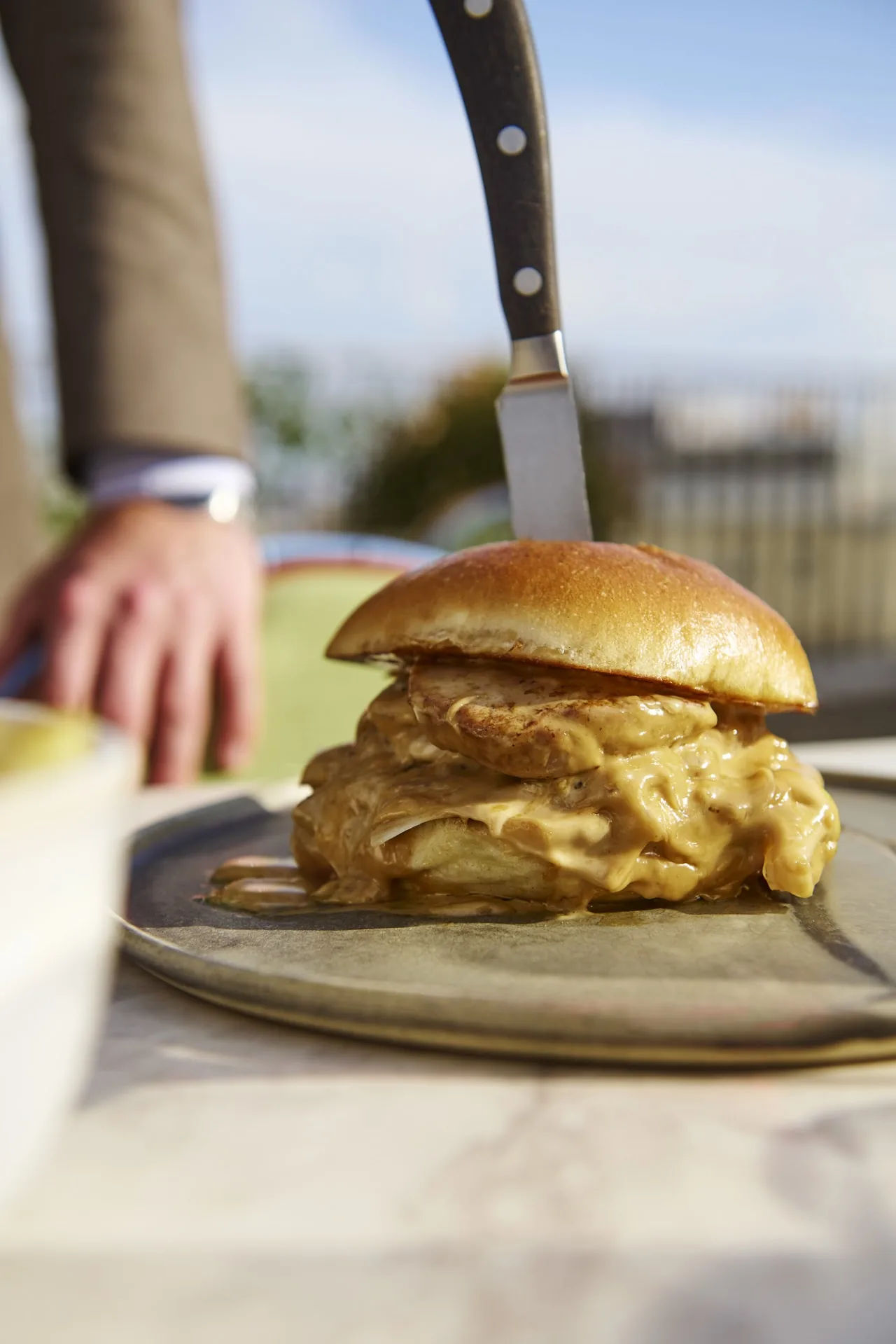 A burger sliced open with a knife driven through it on the plate