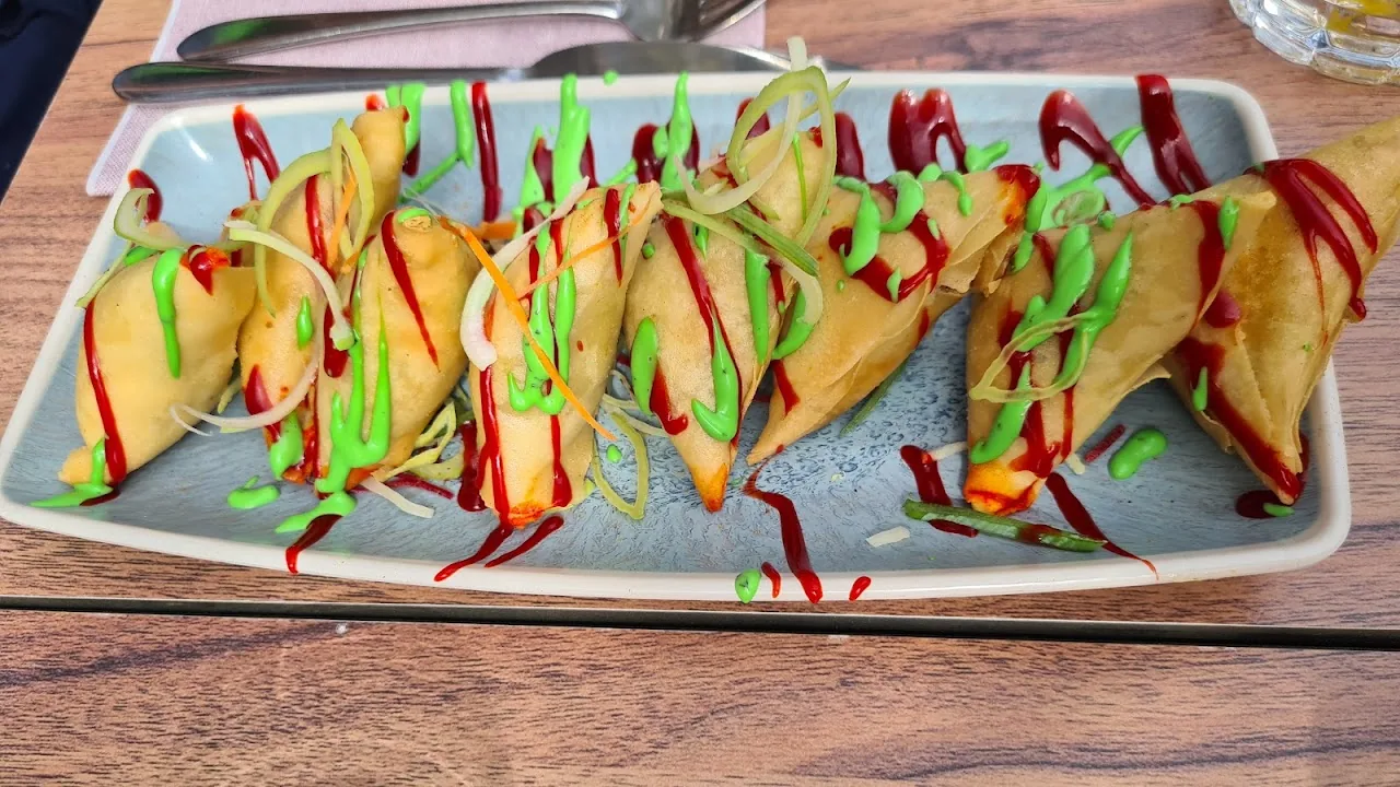 A platter of samosas drizzled with green and red sauce
