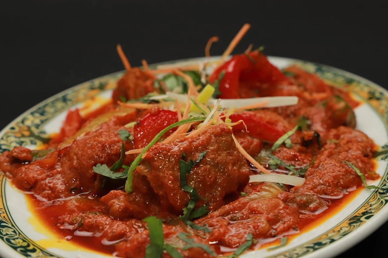 A plate of meat curry in a thick red gravy garnished with herbs