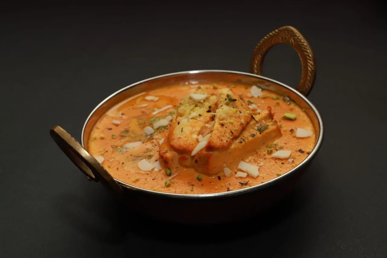A copper bowl of creamy orange curry with paneer cubes