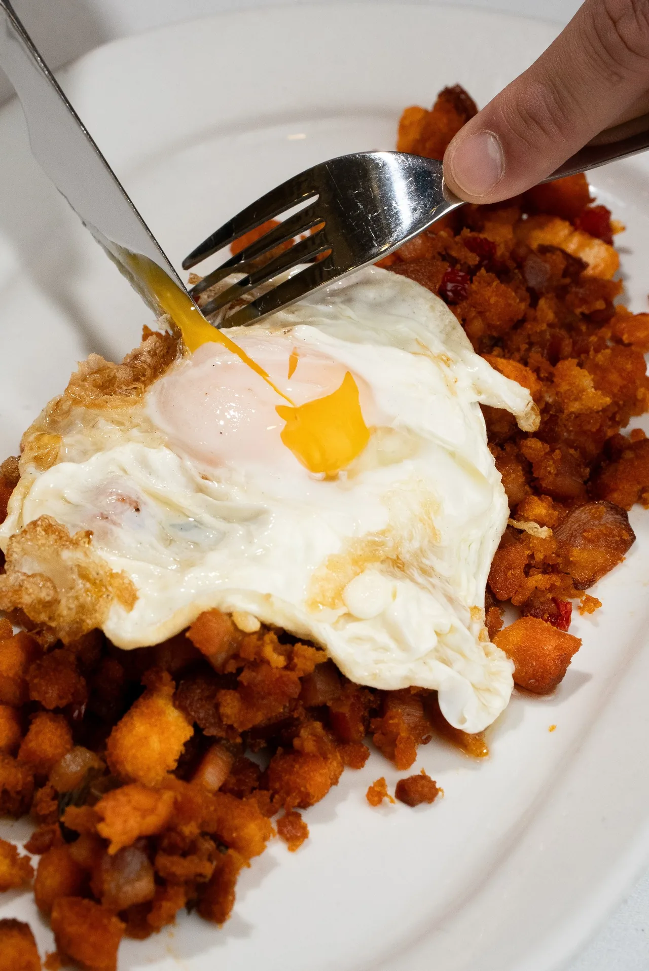 A fried egg on a bed of diced potato and chorizo being cut with a knife and fork