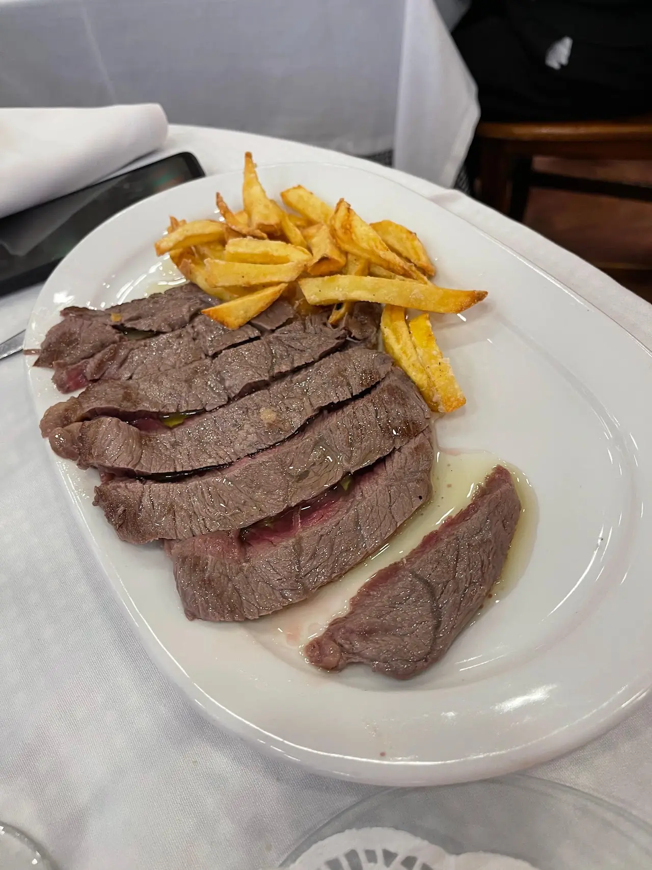 Sliced grilled steak served with french fries on a white plate.