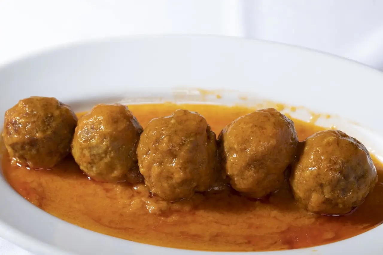 Five meatballs in a reddish tomato sauce on an oval plate.