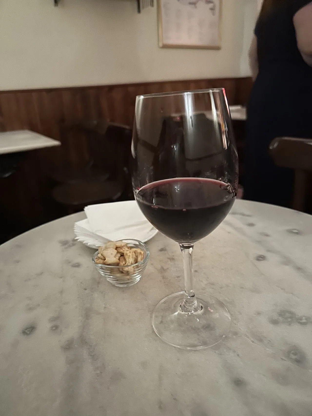 A glass of red wine on a marble table beside a small dish of nuts