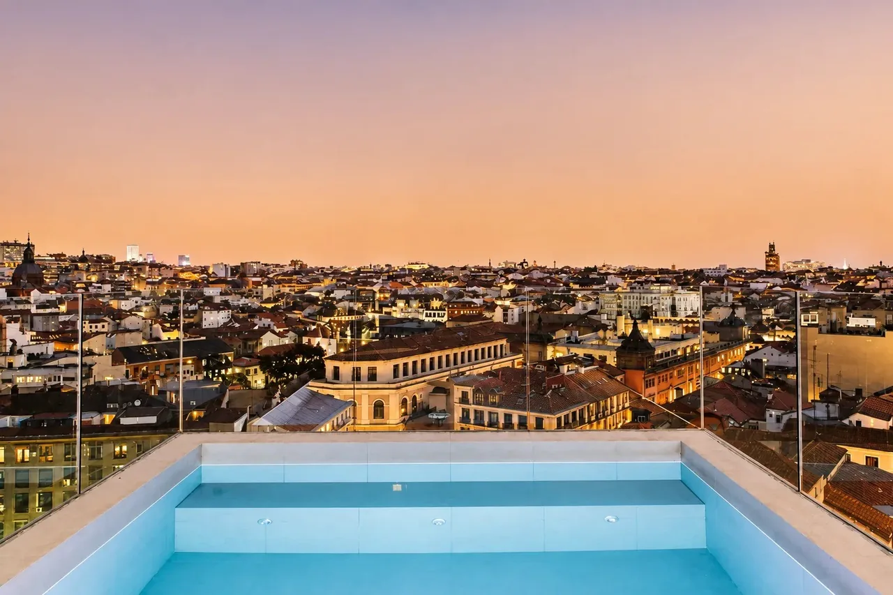 A rooftop plunge pool with the Madrid skyline behind it at sunset