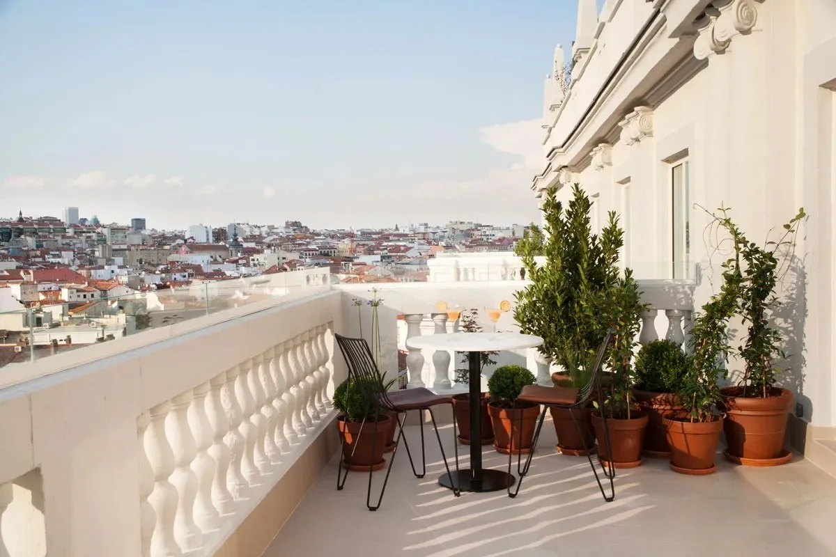 A white balustrade terrace with small tables and potted plants overlooking Madrid