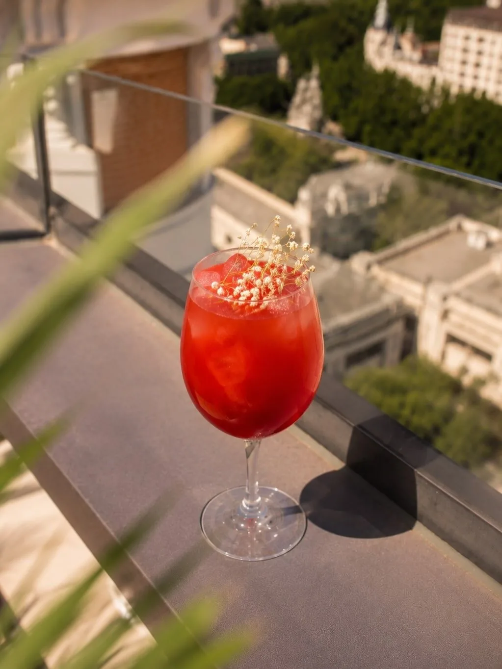 A red cocktail in a stemmed glass on a ledge with buildings far below