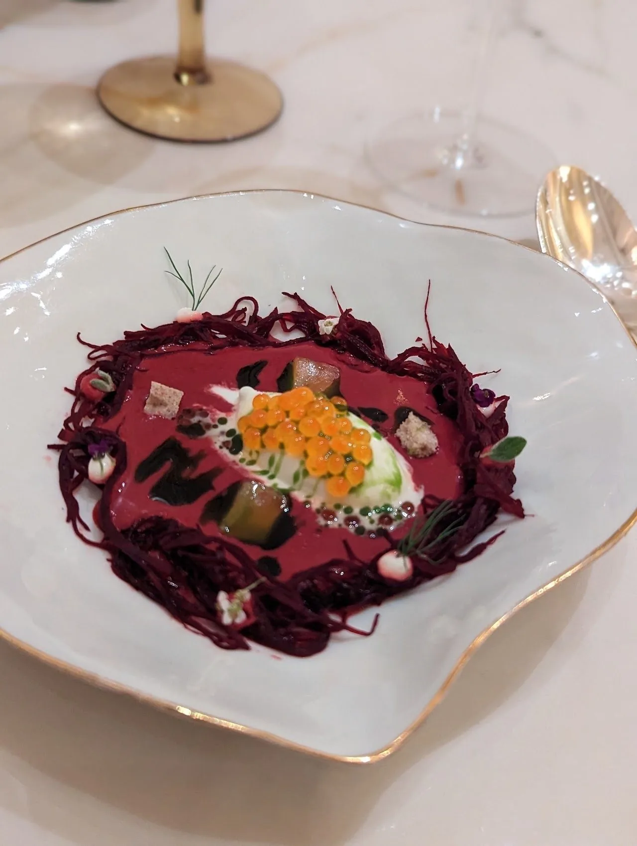 A white plate with a dish of deep red shredded ingredients topped with orange roe on a marble table