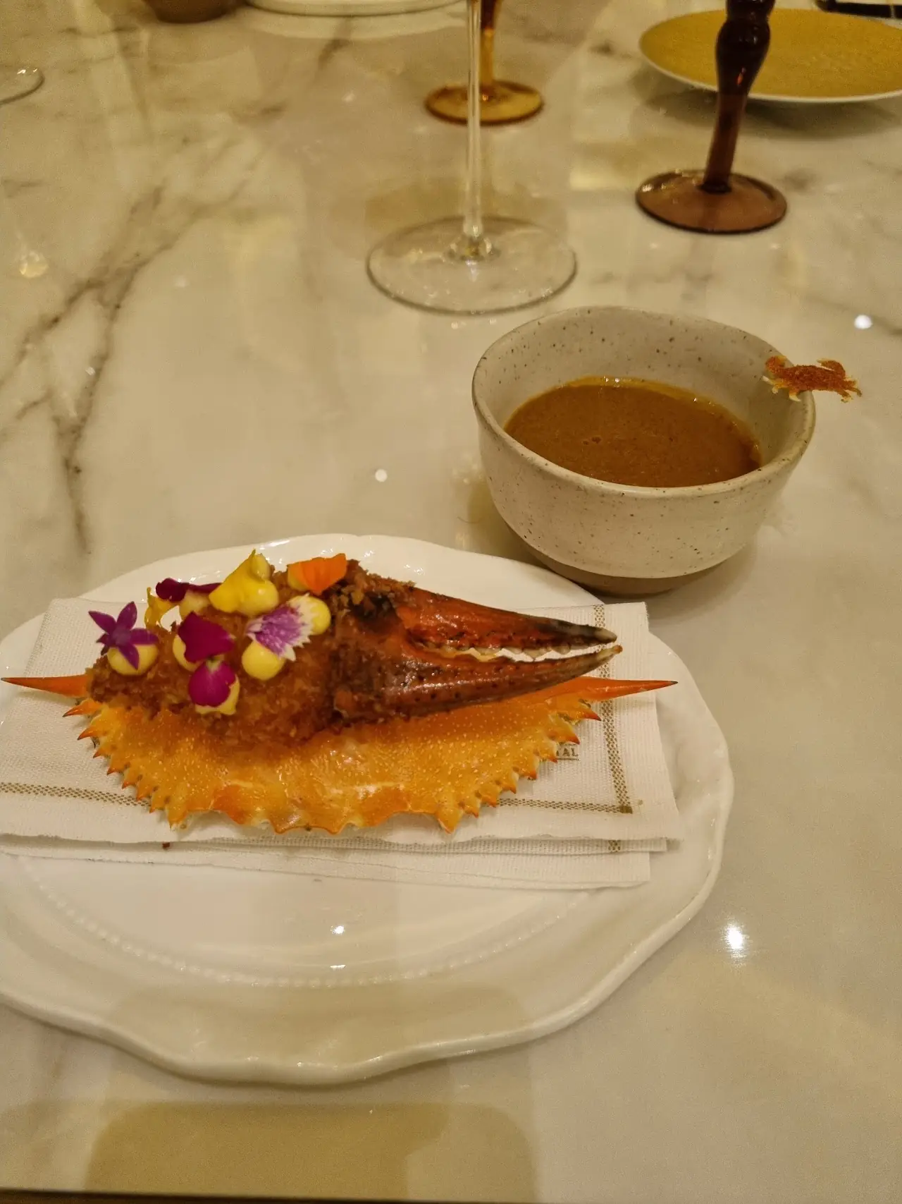 A small fish course on an ornate plate with a cup of sauce alongside
