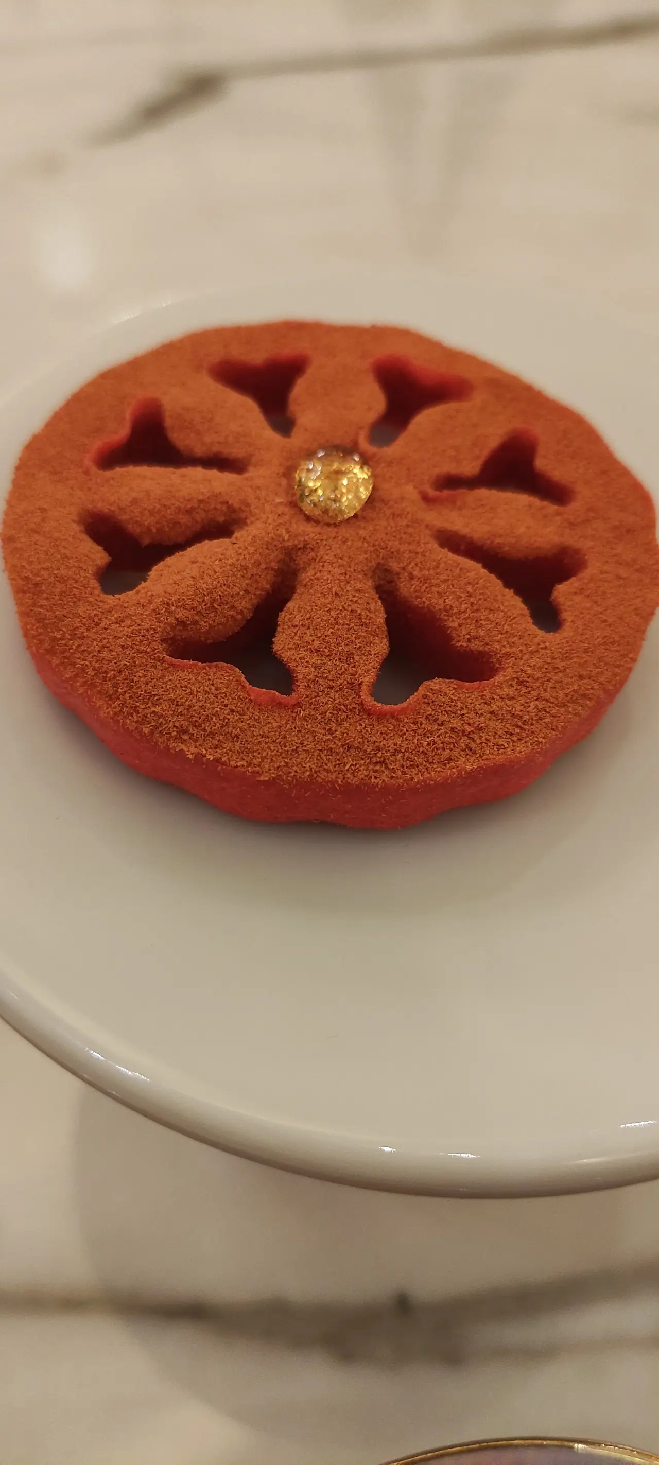 Round red dessert with a petal pattern and a gold dot in the center, on a white plate.