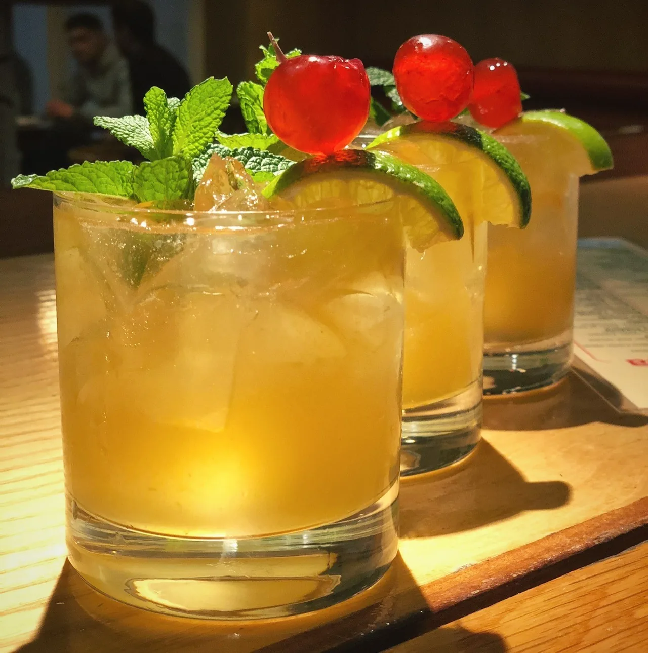 Several cocktails with mint and cherry garnishes on a wooden bar