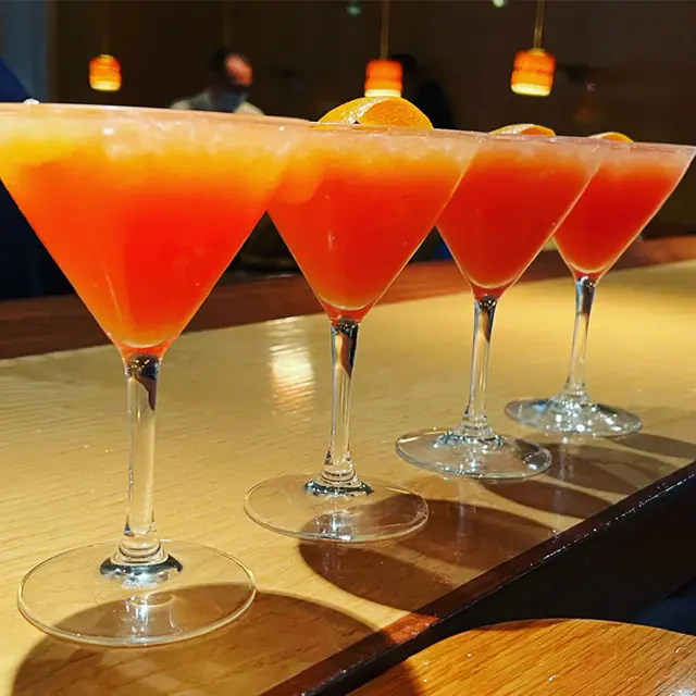 Row of four orange cocktails in martini glasses garnished with orange slices on the bar