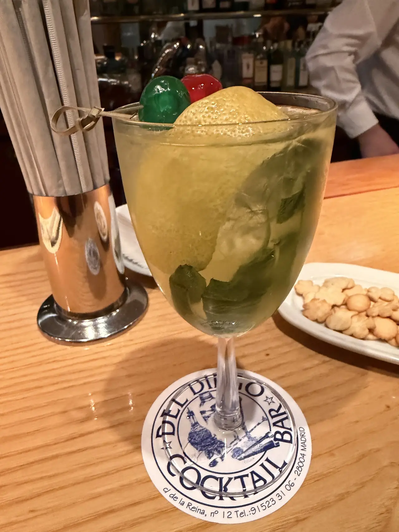 Cocktail with foam top, mint and green and red cherries in a stemmed glass on a Del Diego Cocktail Bar coaster
