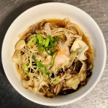Bowl of noodles in broth topped with a soft egg, scallions and bonito flakes