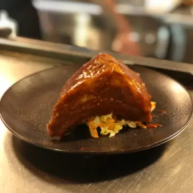 Glazed pork piece served over shredded slaw on a dark plate