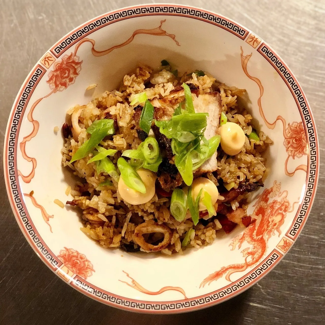 A patterned bowl of fried rice topped with green herbs and cream