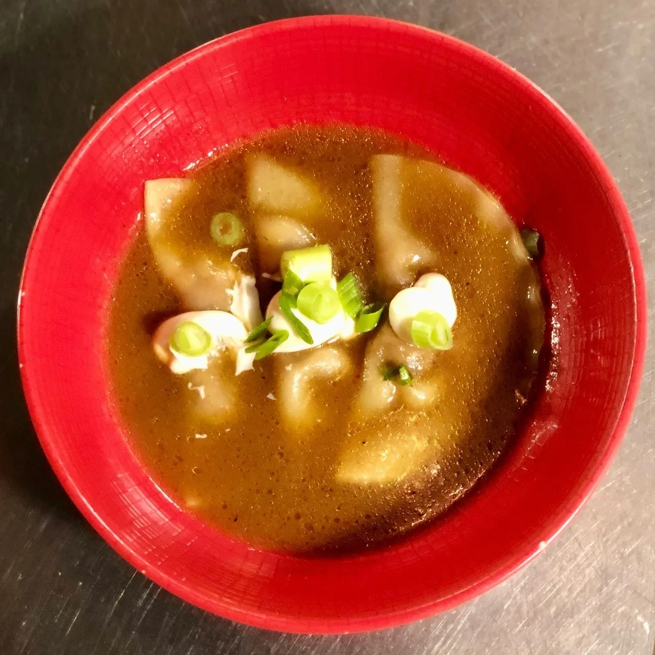 Dumplings in a brown broth in a red bowl