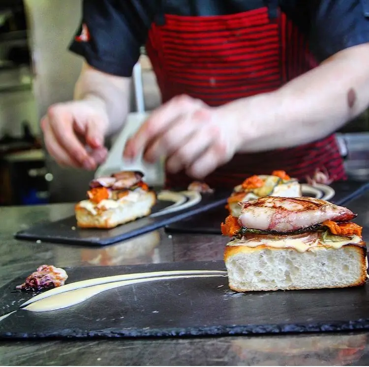 Chef plating open-faced bread topped with seared fish and sauce on slate boards