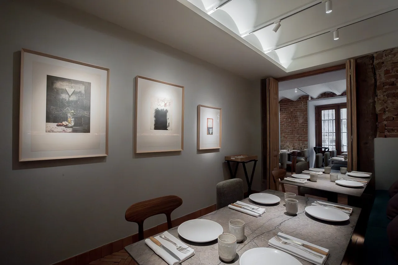 A narrow dining room with framed pictures on the wall and a long table set with plates
