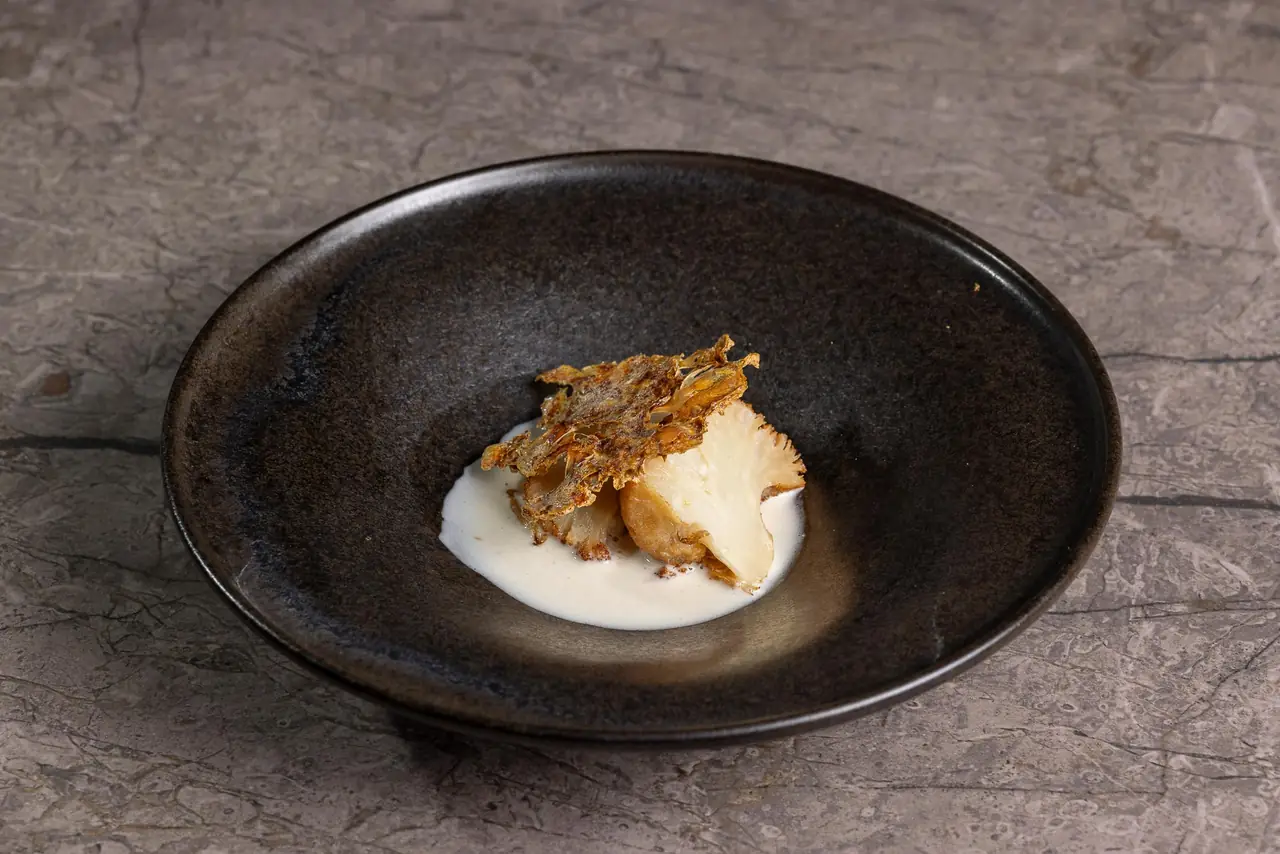 Roasted cauliflower with a crispy leaf over a pale cream sauce in a dark bowl