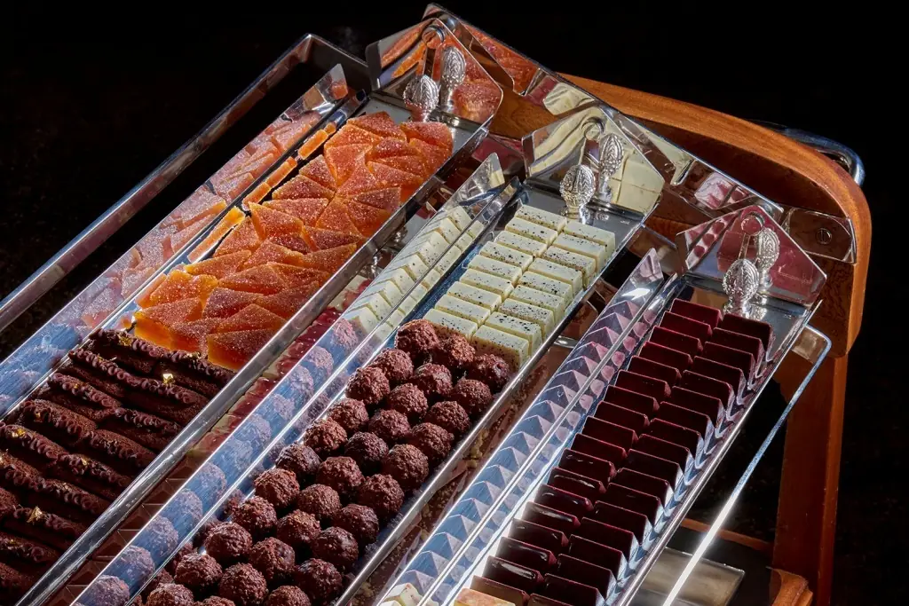 A petit-fours trolley with four mirrored trays holding orange fruit jellies, white chocolate squares, cocoa-dusted truffles and dark ganache batons