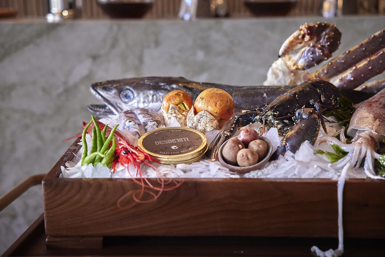 A wooden box of seafood on ice with whole fish, shellfish and a tin of caviar